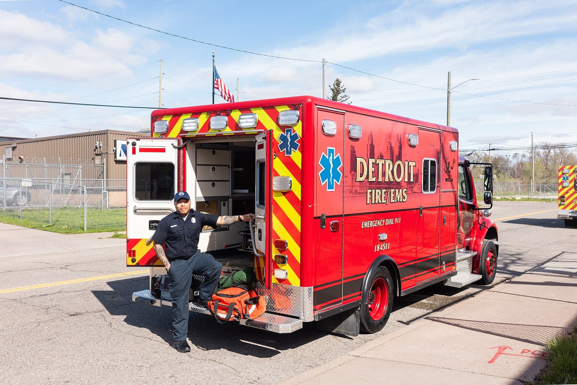 A red Detroit Fire Department EMS ambulance with its side compartment open and a crew member seated at its rear on a sunny day, April 18, 2024. Illustrative image from a City of Detroit photo shoot of the fire department's EMS division; it does not show the Aug. 4 response or the people in this story. Photo: City of Detroit, public domain, via Wikimedia Commons. Source page: https://commons.wikimedia.org/wiki/File:6C5A9225.jpg