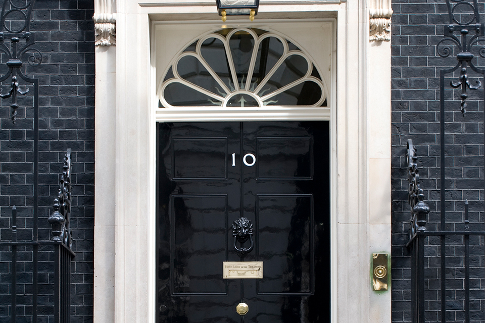 The black front door of 10 Downing Street, with its brass number 10, letterbox and lion's-head knocker, set in a dark brick facade.