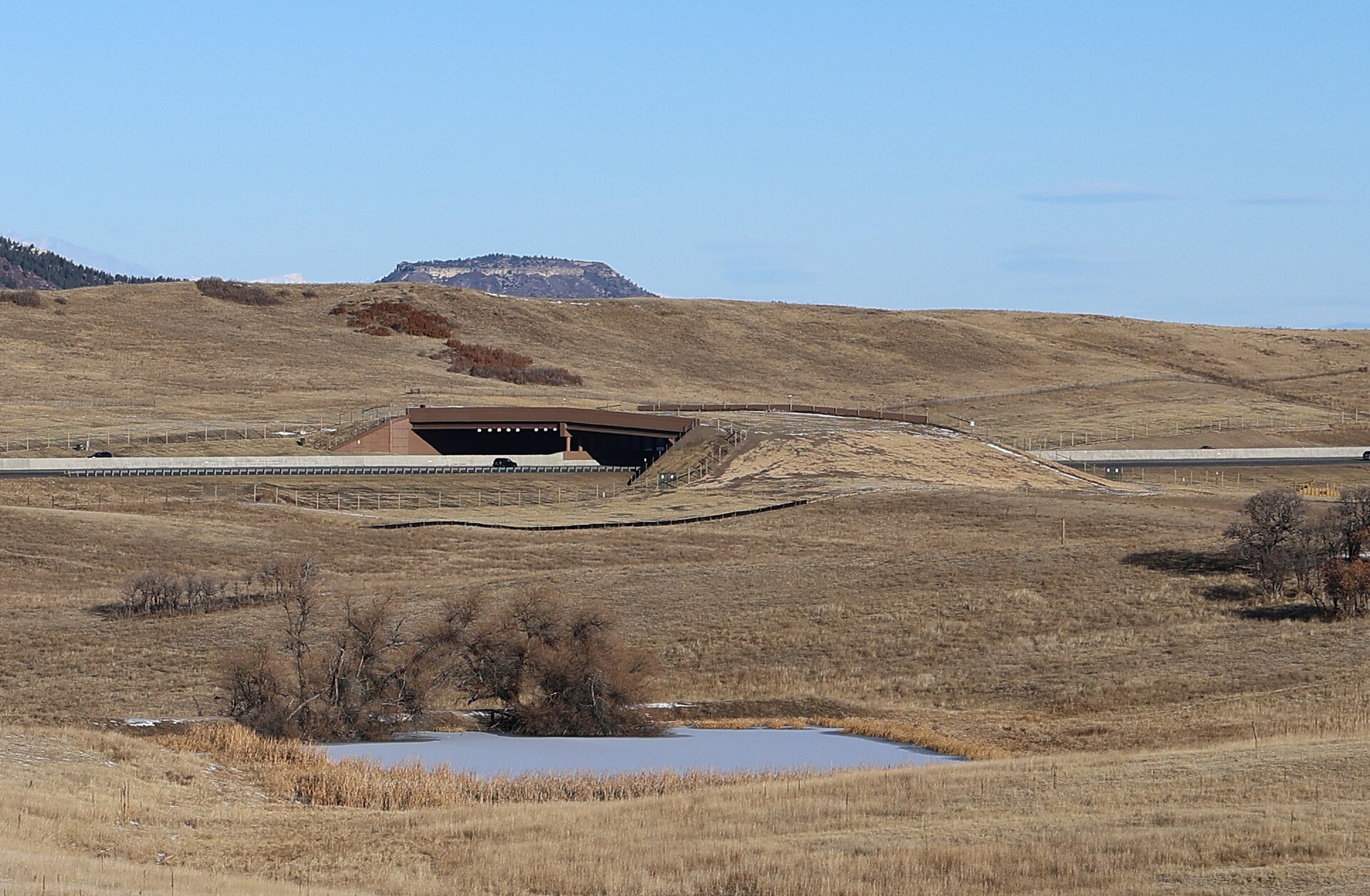 Greenland wildlife overpass with pond and fencing in the foreground.