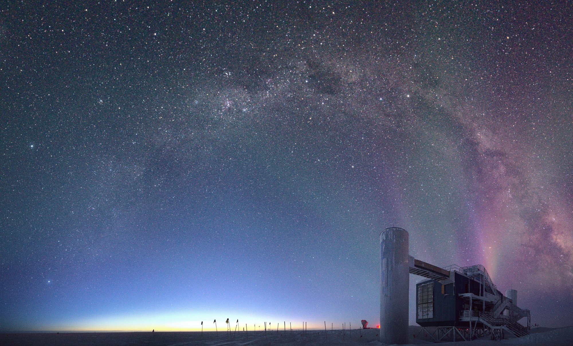 A tall, boxy research building on a flat expanse of snow at twilight, beneath a sky full of stars, the Milky Way and faint auroras.