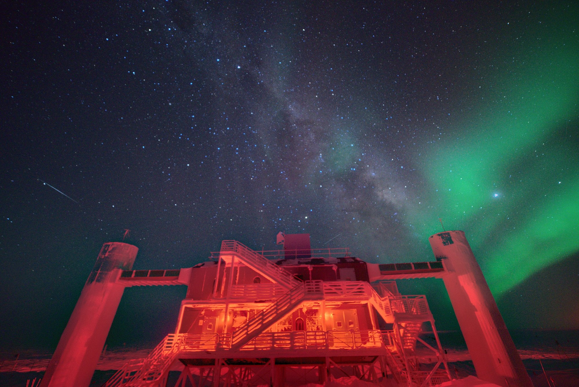 A research building lit red by safety lights at night, with green auroras and a starry sky overhead.