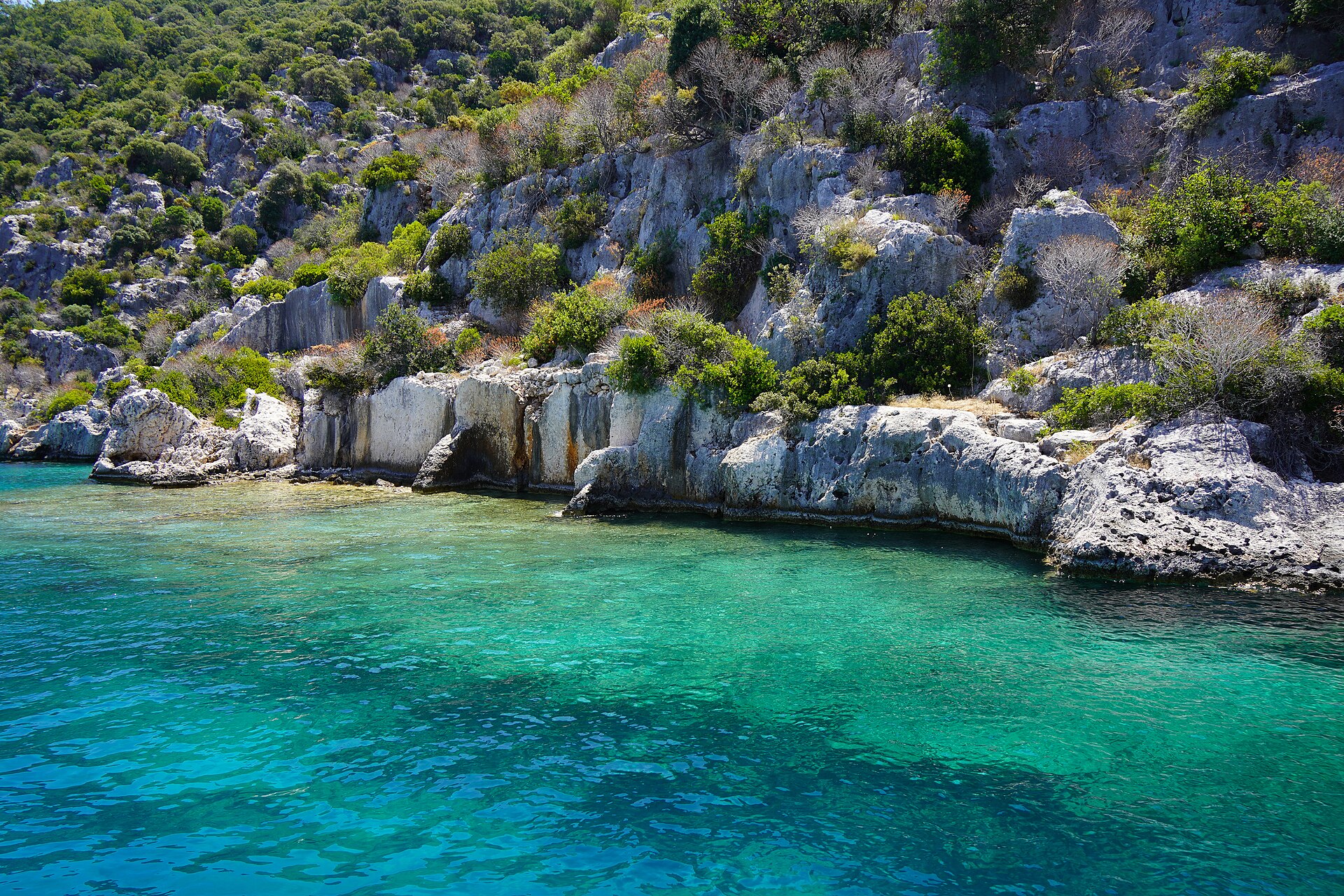 Clear turquoise water lapping against pale limestone rocks and ancient stone ruins along the Kekova shoreline.