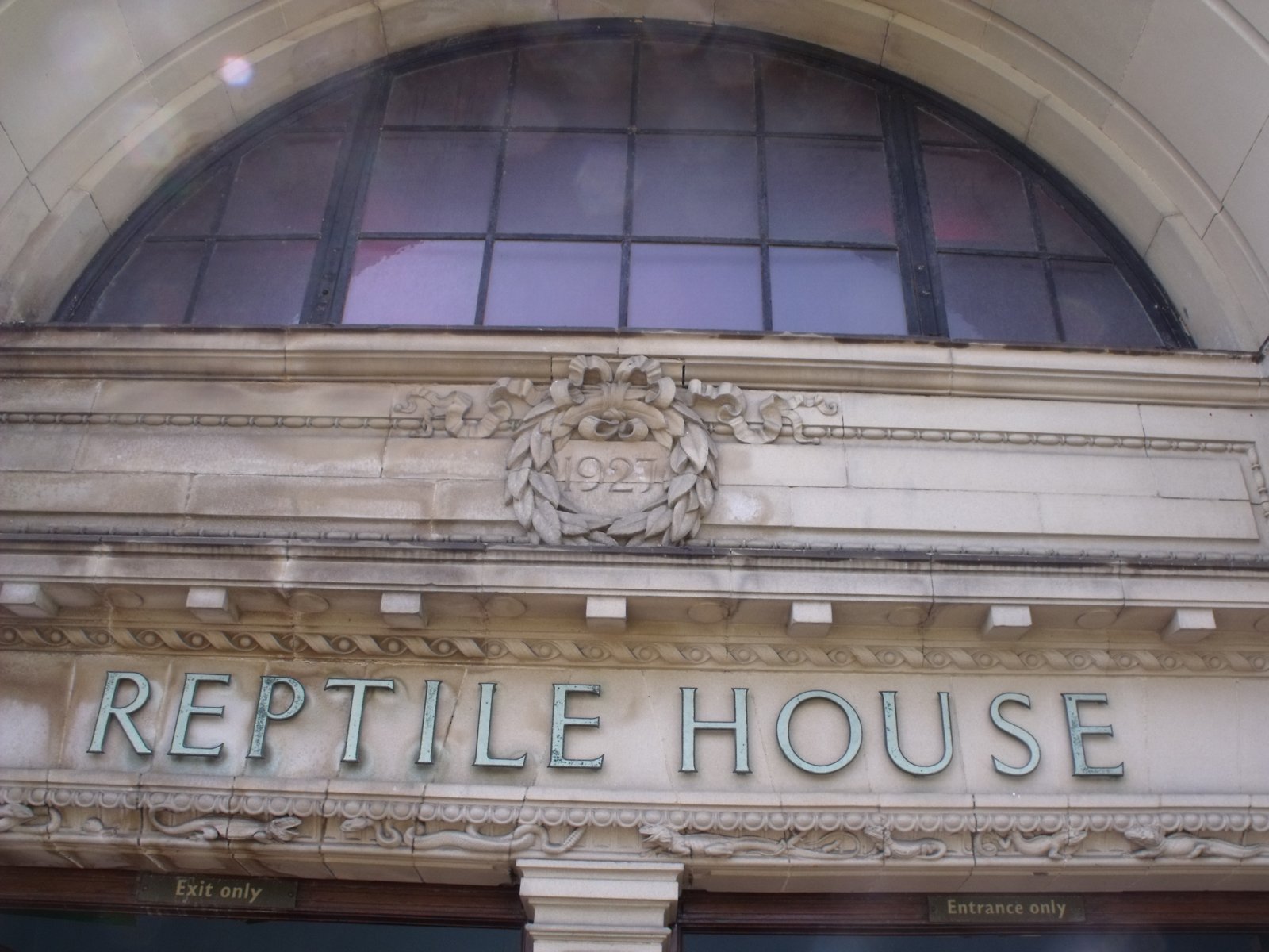 An arched window above a carved 1927 date crest and the lettering Reptile House on a stone facade.