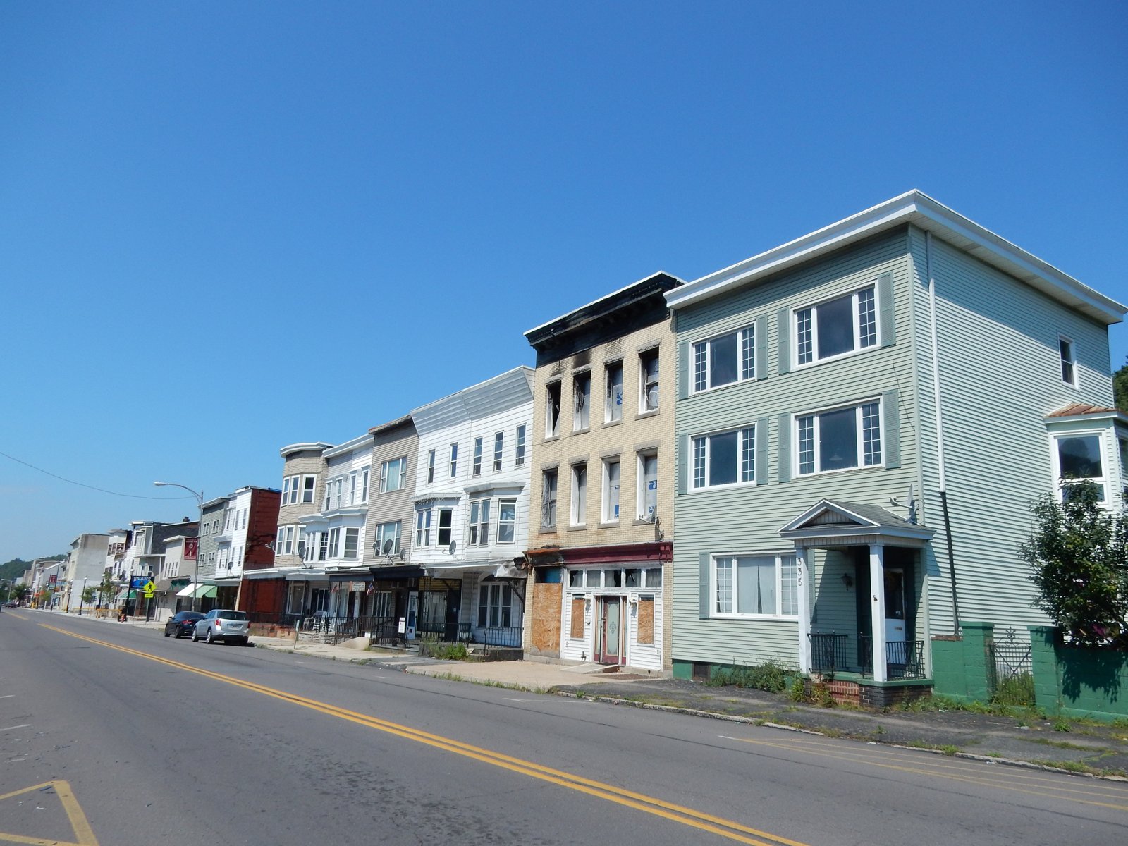 East Centre Street in Mahanoy City, Pennsylvania, lined with row houses and storefronts under a clear blue sky, looking west from 4th Street.
