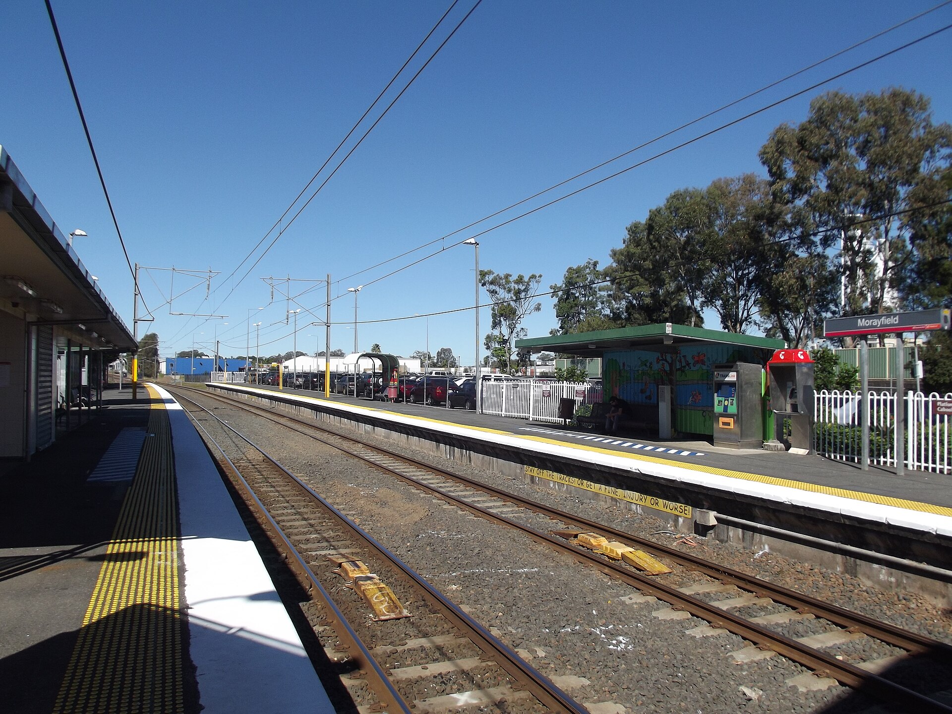 The platforms and overhead wires of Morayfield railway station in Queensland on a clear day.