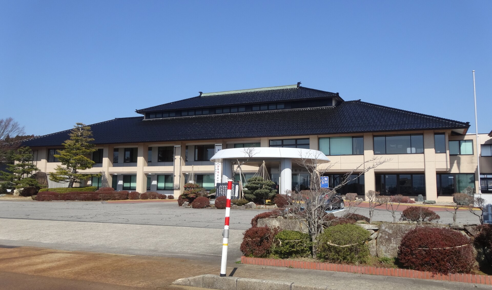 A modern low municipal building with a parking area in front under a clear sky.