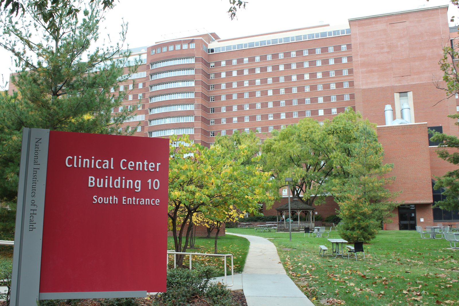 The south entrance of the NIH Clinical Center, a large modern building with a glass facade, on the National Institutes of Health campus in Bethesda, Maryland.