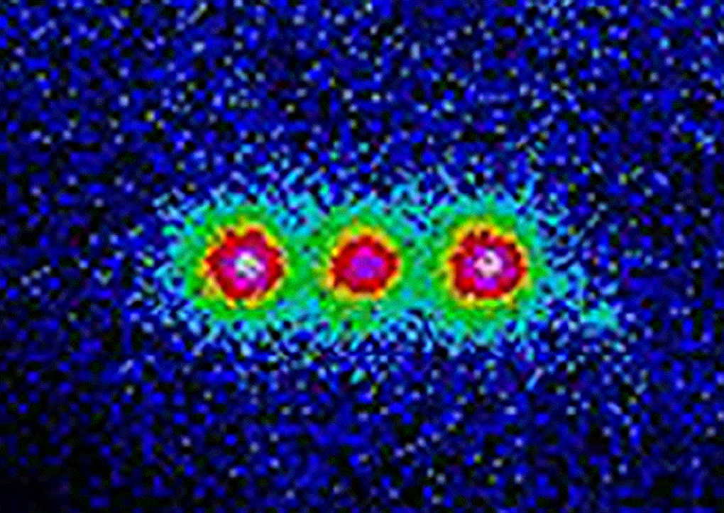 A colorized image of three glowing spots in a row, the fluorescence of three trapped ions.