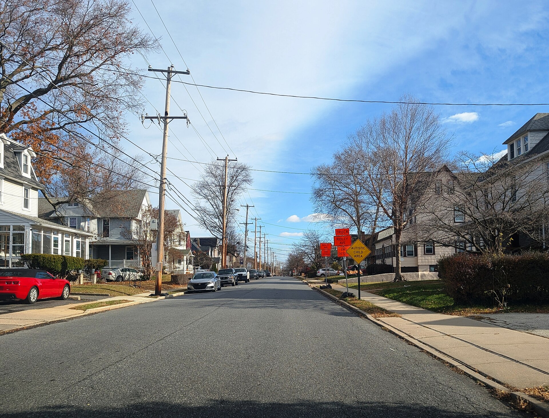 A quiet residential street lined with houses, utility poles and bare trees under a blue sky.