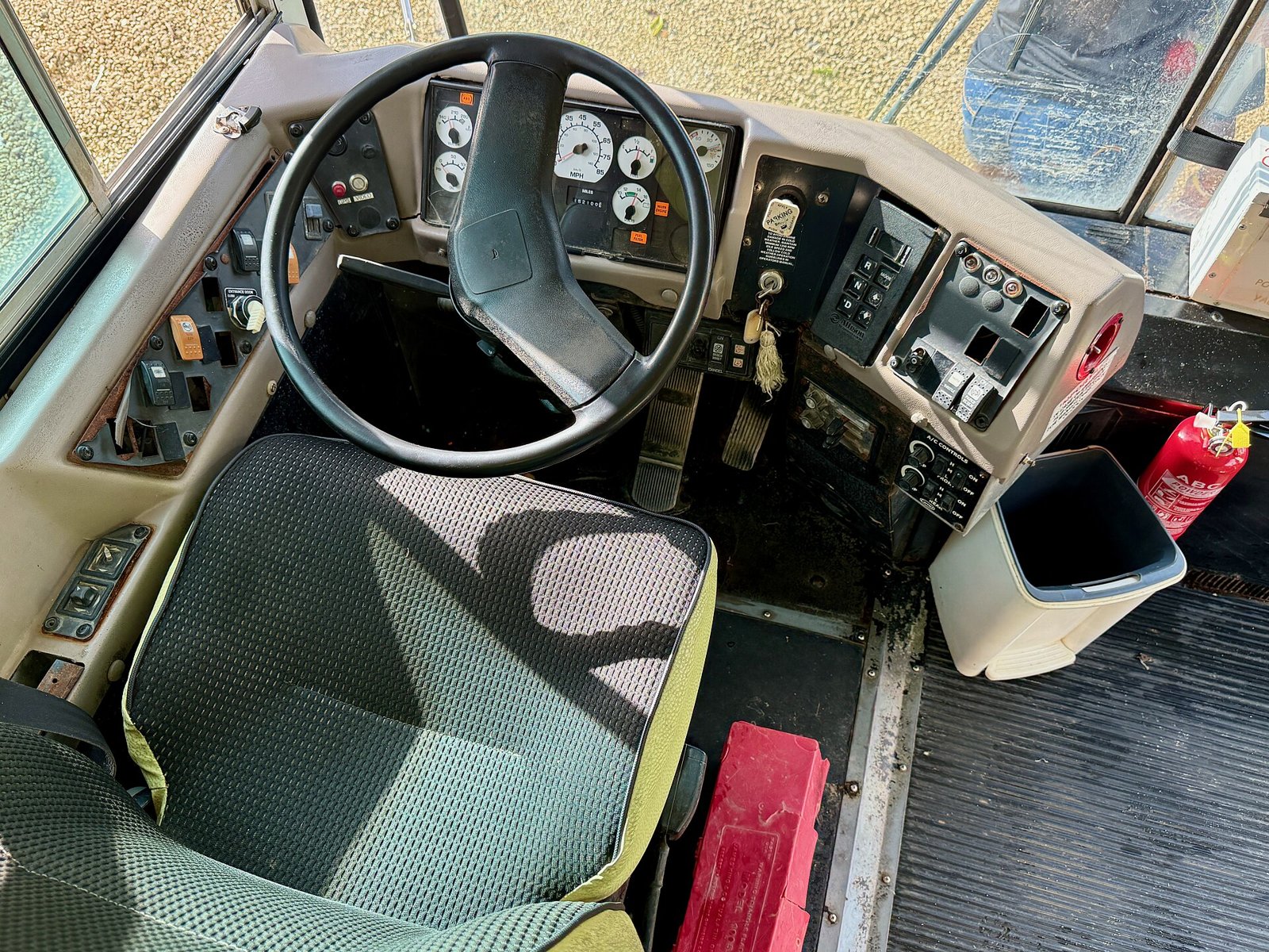 The driver's seat, steering wheel, gauges and switch panels of a school bus, seen from above and behind.