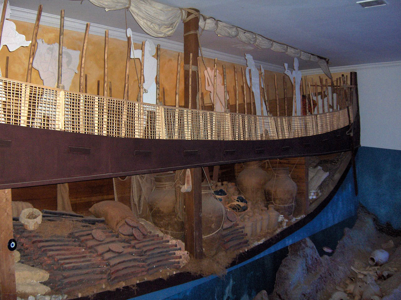 A full-size wooden replica of an ancient ship's hull with a cargo of jars, displayed in a museum hall.